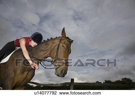 Stock Image - Female horseback rider embracing horse. Fotosearch