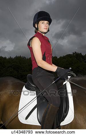 Stock Image - Female horseback rider sitting on brown horse. Fotosearch