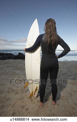 Female surfer standing holding surfboard on beach back view View Large Photo Image Picture - Female surfer standing holding surfboard on beach back view. Fotosearch