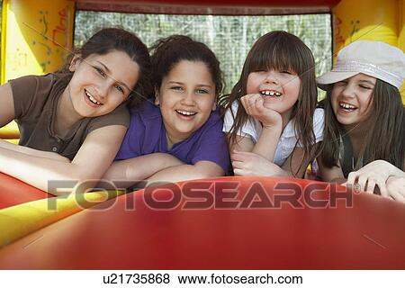 Stock Photo - Four girls (7-12) lying in row in bouncy castle laughing portrait. Fotosearch