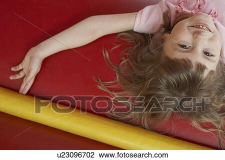 Stock Image - Girl (5-6) lying down in bouncy castle portrait close up view from above. Fotosearch