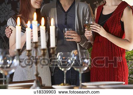 Stock Image - Group of people holding wine glasses standing by dining table mid section. Fotosearch