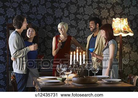 Stock Image - Group of people smiling standing by dining table. Fotosearch