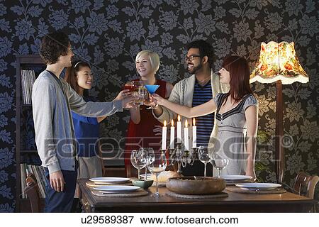 Stock Photo - Group of people toasting standing by dining table. Fotosearch