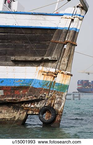 Stock Image - Khor Fakkan UAE old wooden dhow washed up on shore in front of Khor Fakkport. Fotosearch