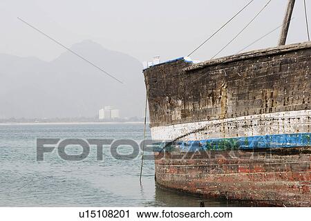 Stock Image - Khor Fakkan UAE old wooden dhow washed up on shore in front of Khor Fakkport. Fotosearch