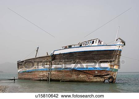 Stock Image - Khor Fakkan UAE old wooden dhow washed up on shore. Fotosearch