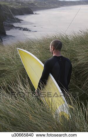 Man carrying surfboard down hill torwards sea back view View Large Photo Image Stock Image - Man carrying surfboard down hill torwards sea back view. Fotosearch