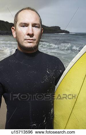 Stock Photograph - Man holding surfboard on beach close up portrait. Fotosearch