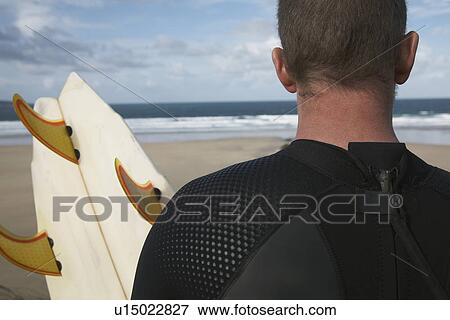 Man holding surfboard on beach looking at sea back view close up View Large Photo Image Stock Photo - Man holding surfboard on beach looking at sea back view close up. Fotosearch