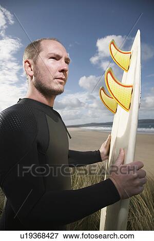 Man holding surfboard on beach View Large Photo Image Stock Photo - Man holding surfboard on beach. Fotosearch