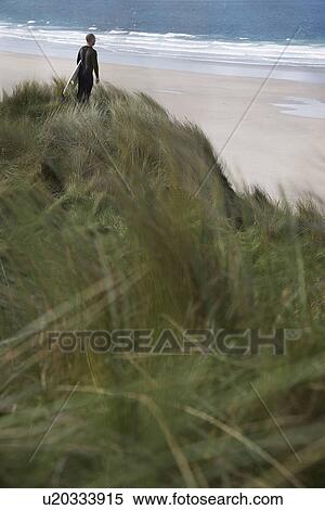 Stock Photography - Man holding surfboard on cliff looking at sea back view. Fotosearch