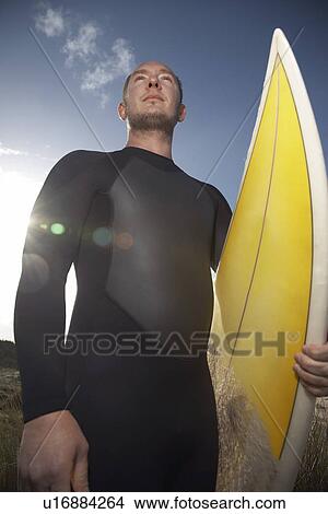 Picture - Man holding surfboard standing on beach low angle view. Fotosearch