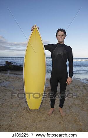 Stock Photo - Man holding surfboard standing on beach portrait. Fotosearch