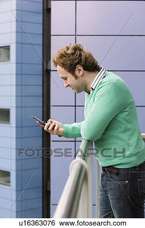 Stock Photograph - Man text messaging on balcony side view. Fotosearch