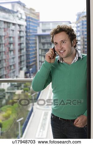 Stock Image - Man using mobile phone on balcony. Fotosearch