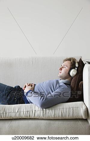 Man wearing headphones lying on sofa in living room side view View Large Photo Image Stock Image - Man wearing headphones lying on sofa in living room side view. Fotosearch