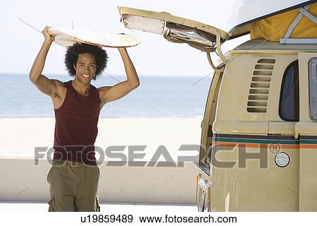 Stock Photo - Man with surfboard by camper van. Fotosearch