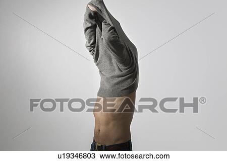 Stock Image - Mid-adult man pulling sweater over head. Fotosearch