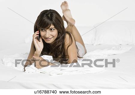 Stock Image - Mid adult woman lying on bed and talking on phone. Fotosearch