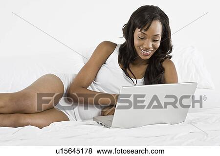 Mid adult woman lying on bed and using laptop View Large Photo Image Stock Photo - Mid adult woman lying on bed and using laptop. Fotosearch