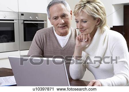 Middle-aged couple counting bills using laptop in kitchen View Large Photo Image Stock Image - Middle-aged couple counting bills using laptop in kitchen. Fotosearch