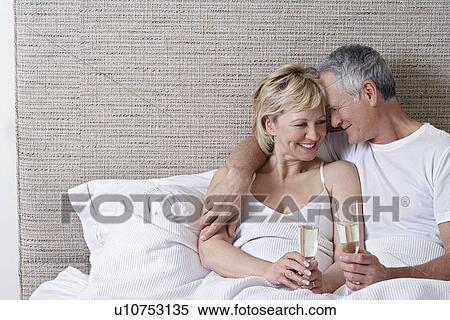 Stock Photography - Middle-aged couple drinking champagne in bed. Fotosearch