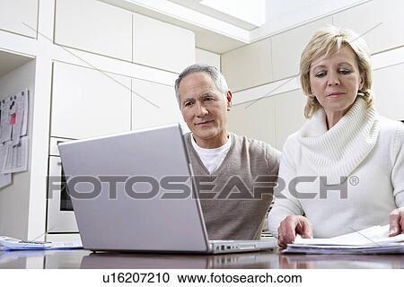 Middle-aged couple working on laptop in kitchen View Large Photo Image Stock Image - Middle-aged couple working on laptop in kitchen. Fotosearch