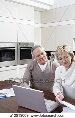 Middle-aged couple working on laptop in kitchen View Large Photo Image Stock Photo - Middle-aged couple working on laptop in kitchen. Fotosearch