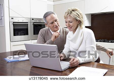 Middle-aged couple working on laptop in kitchen View Large Photo Image Stock Photography - Middle-aged couple working on laptop in kitchen. Fotosearch