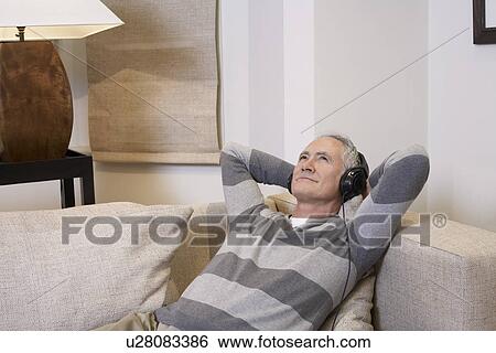 Stock Photograph - Middle-aged man listentening to music on headphones in living room. Fotosearch