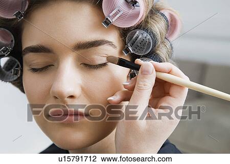 Stock Image - Model in Hair Curlers Having Makeup Applied. Fotosearch