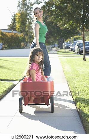 Stock Image - Mother pulling daughter in trolley. Fotosearch