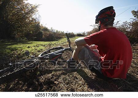 Mountain biker sitting beside bike in countryside View Large Photo Image Stock Photo - Mountain biker sitting beside bike in countryside. Fotosearch