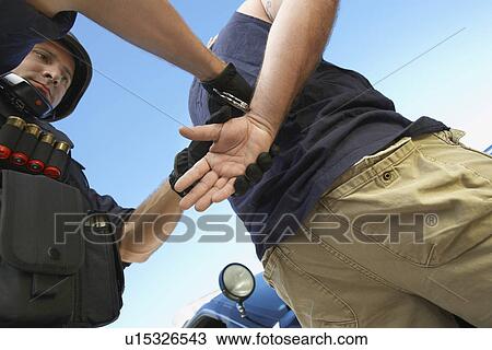 Stock Image - Police man putting handcuffs on criminal. Fotosearch