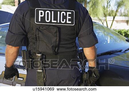 Stock Photo - Police officer in bulletproof vest outdoors back view. Fotosearch