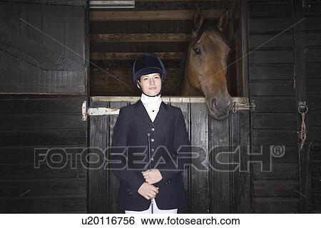 Stock Photograph - Portrait of Female horseback rider with horse in stable. Fotosearch
