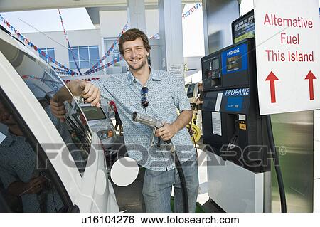 Stock Photograph - Portrait of smiling man refueling car at natural gas station. Fotosearch