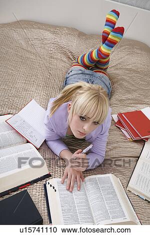 Stock Image - Portrait of teenage girl (16-17) doing homework on bed. Fotosearch