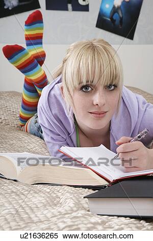 Stock Photography - Portrait of teenage girl (16-17) doing homework on bed. Fotosearch