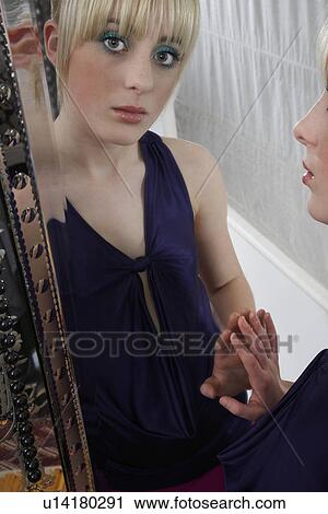 Stock Image - Portrait of teenage girl (16-17) in elegant dress looking in mirror. Fotosearch