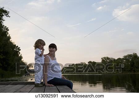 Pregnant Mother And Daughter Sitting On Jetty In Evening View Large Photo Image Stock Image - Pregnant Mother And Daughter Sitting On Jetty In Evening. Fotosearch