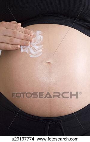 Pregnant woman applying cream to stomach mid section View Large Photo Image Picture - Pregnant woman applying cream to stomach mid section. Fotosearch