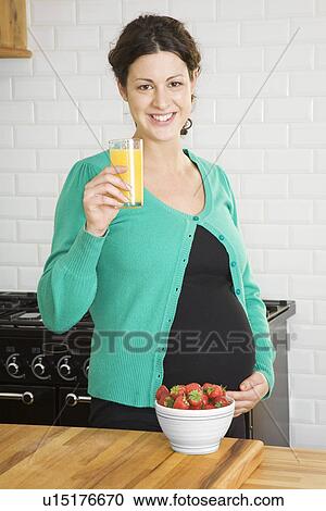 Stock Image - Pregnant woman drinking fruit juice in kitchen portrait. Fotosearch