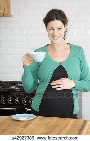 Stock Photograph - Pregnant woman drinking tea in kitchen. Fotosearch