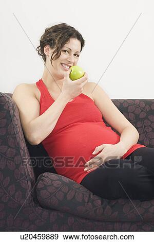 Pregnant woman eating apple on sofa portrait View Large Photo Image Stock Photo - Pregnant woman eating apple on sofa portrait. Fotosearch