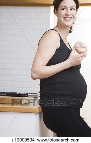 Pregnant woman eating doughnut in kitchen View Large Photo Image Picture - Pregnant woman eating doughnut in kitchen. Fotosearch