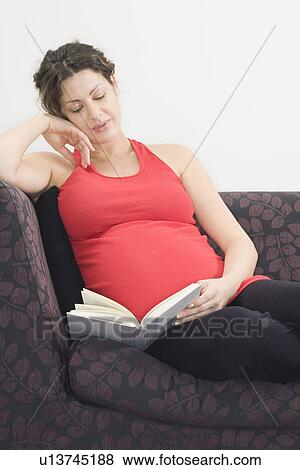 Stock Photo - Pregnant woman reading on sofa. Fotosearch