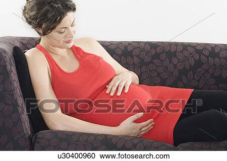 Stock Image - Pregnant woman relaxing on sofa. Fotosearch