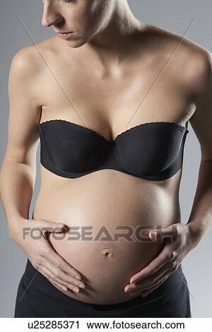 Stock Image - Pregnant woman touching abdomen studio shot. Fotosearch